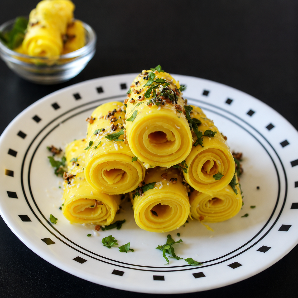 Gluten-free khandvi rolls garnished with sesame seeds, mustard seeds, and fresh coriander on a white plate.