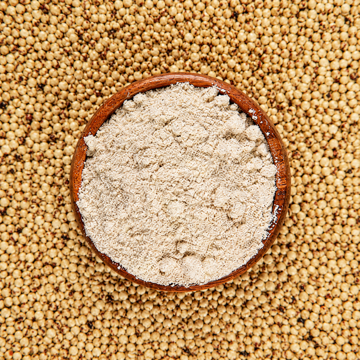 Overhead view of gluten-free flour in a wooden bowl surrounded by whole grains on a rustic background, showcasing its fine texture and natural ingredients.
