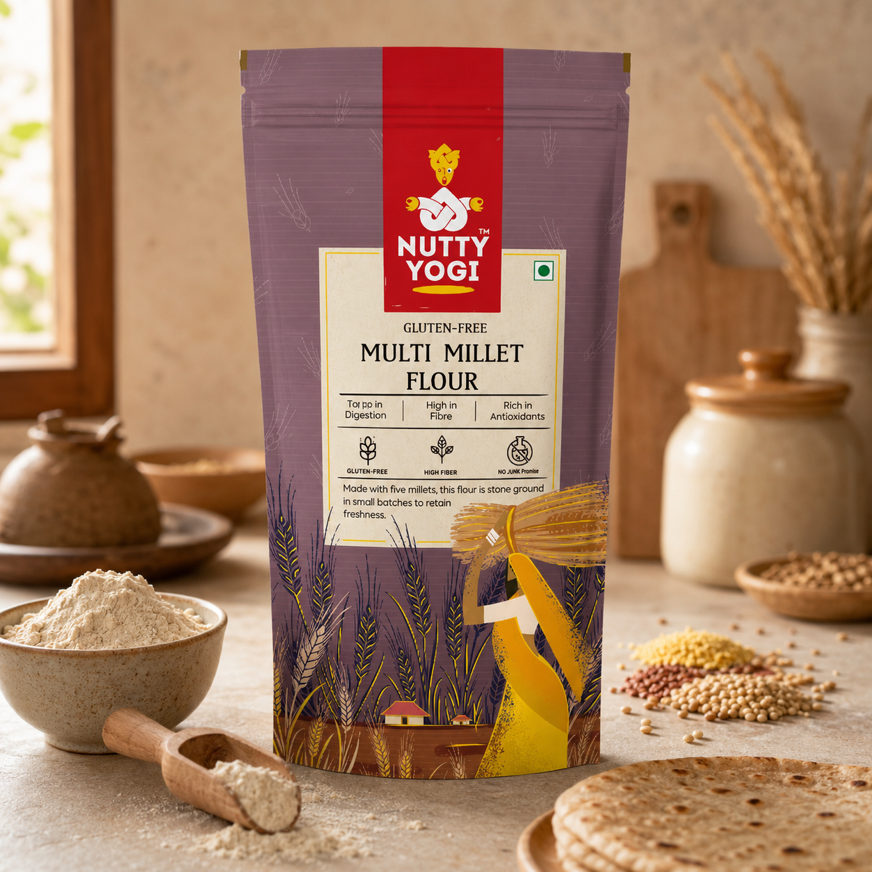 A stand-up pouch of Nutty Yogi Gluten-Free Multi Millet Flour is centered on a rustic kitchen counter with bowls of flour, a wooden spoon, wheat, and flatbread. The package is purple with a red brand panel and yellow wheat illustrations.