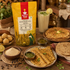 A bag of Nutty Yogi Black Chana Atta (Sattu) is displayed on a rustic wooden table surrounded by prepared food, including flatbreads, a glass of milk drink, and bowls of seasoning, creating a warm, appetizing scene.