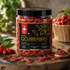A 200g jar of Nutty Yogi Dried Gojiberry on a rustic wooden table, surrounded by fresh gojiberry berries, leaves, and a wooden spoon with scattered dried berries.