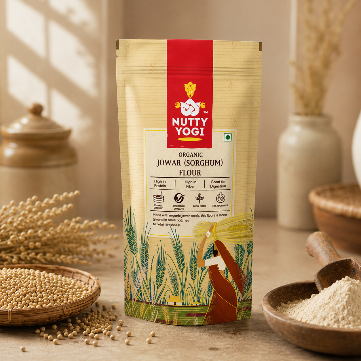 A stand-up pouch of Nutty Yogi Organic Jowar (Sorghum) Flour stands on a wooden surface with wheat, seeds, and flour bowls around it in a warm, rustic setting.