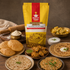 A bag of Nutty Yogi Farali Atta (Vrat Ka Atta) stands prominently in the center of a styled Indian food spread on a rustic wooden table, surrounded by flatbreads, fried snacks, chutney, and a rolling pin.