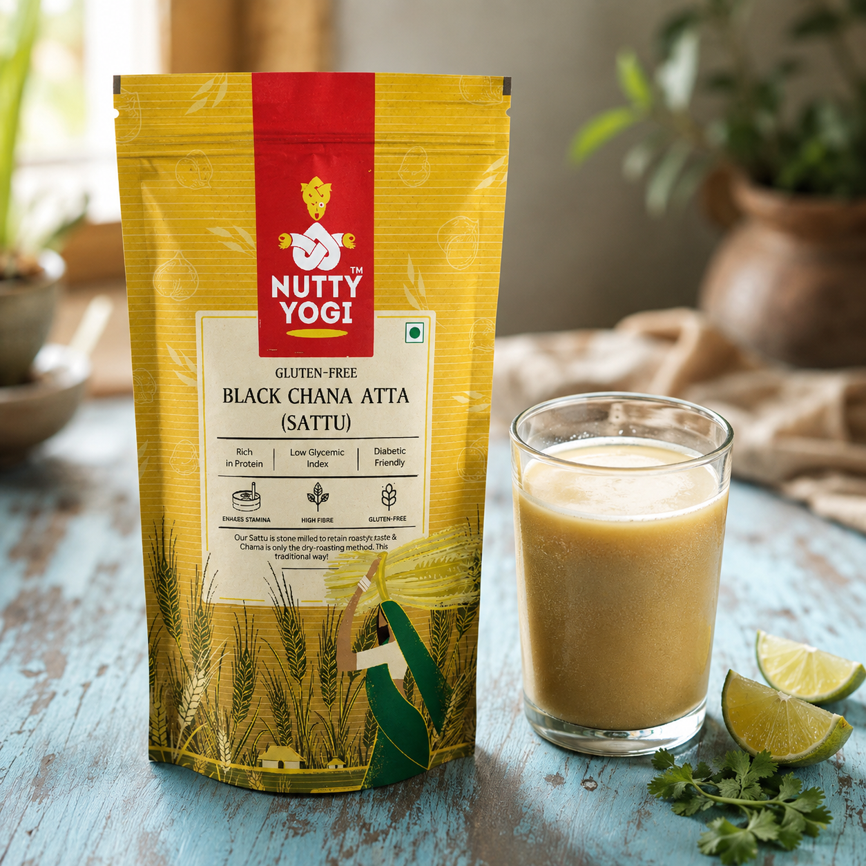 A stand-up pouch of Nutty Yogi Black Ghana Atta (Sattu) next to a glass of the prepared beige drink, with lime wedges and cilantro on a rustic blue wooden table.