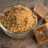 Close-up of natural jaggery powder in a glass bowl with jaggery cubes, highlighting its unrefined texture and natural sweetness.