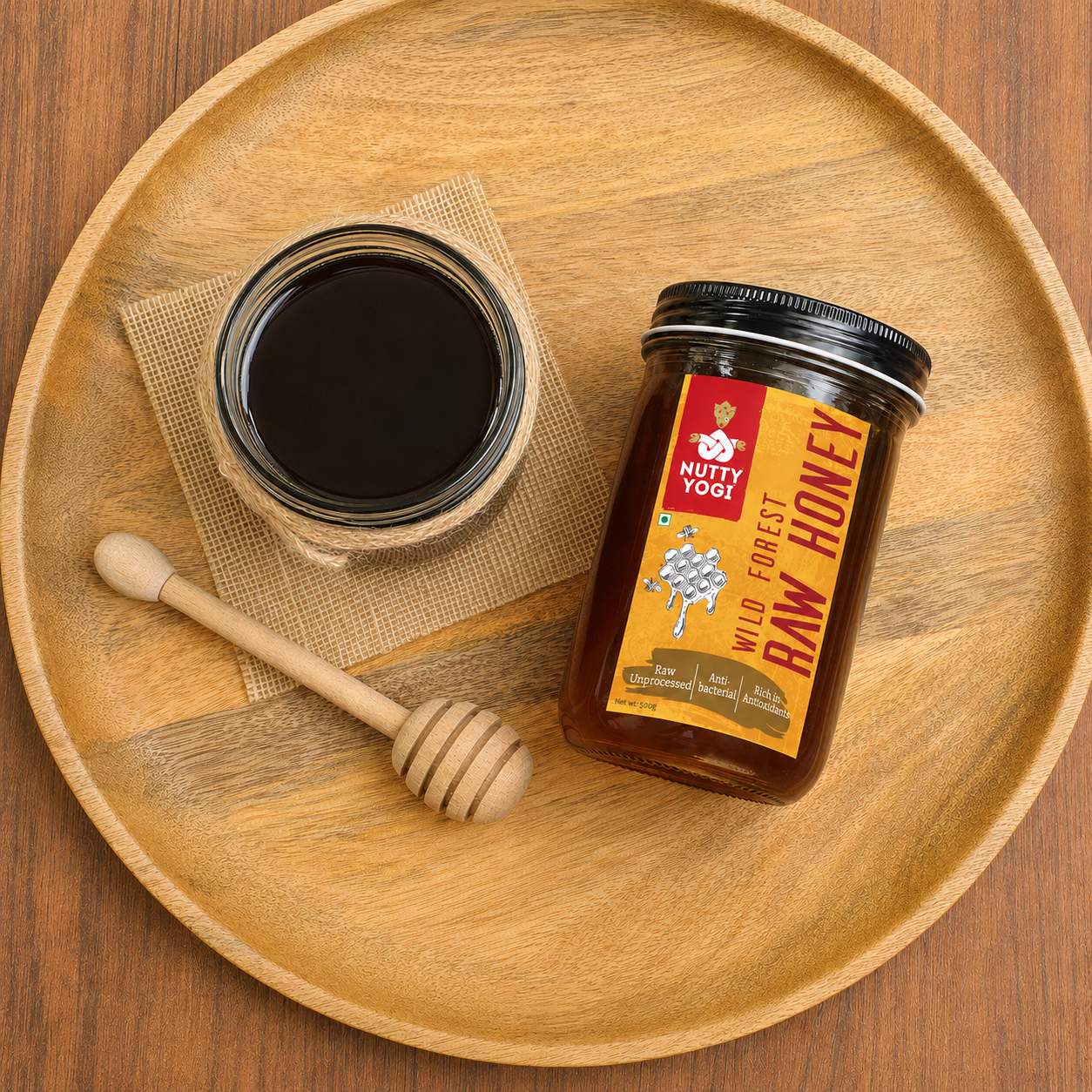 Nutty Yogi Wild Forest Raw Honey jar with a bowl of raw honey and wooden honey dipper on a wooden serving tray

