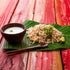 Sabudana khichdi served on a fresh banana leaf with a bowl of yogurt, wooden spoon, and lemon wedge on a rustic wooden table, creating a traditional Indian meal presentation.
