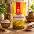 A bag of Nutty Yogi Sprouted Ragi Flour stands on a wooden table surrounded by bowls of flour, red ragi seeds, and kitchen decor in a warm, rustic setting.