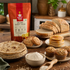 A bag of Nutty Yog! Organic Barley Flour stands on a rustic wooden table surrounded by baked goods made from the flour, including flatbreads, pancakes, muffins, and bread slices. The scene is styled with bowls, a spoon, and warm kitchen props in the background.