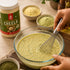 Person whisking a bowl of green mixture with Nutty Yogi Power Protein Cheela container in the background.